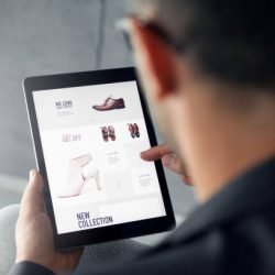 Male hand is browsing an online shop on digital tablet which is selling shoes.